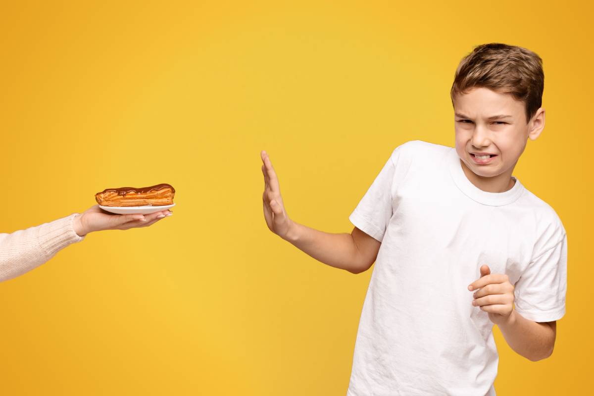 Boy Rejecting a Hotdog Offered by an Adult on a Yellow Background