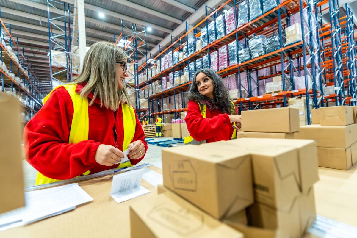 Two caucasian adult women working together organizing shipments in a distribution warehouse
